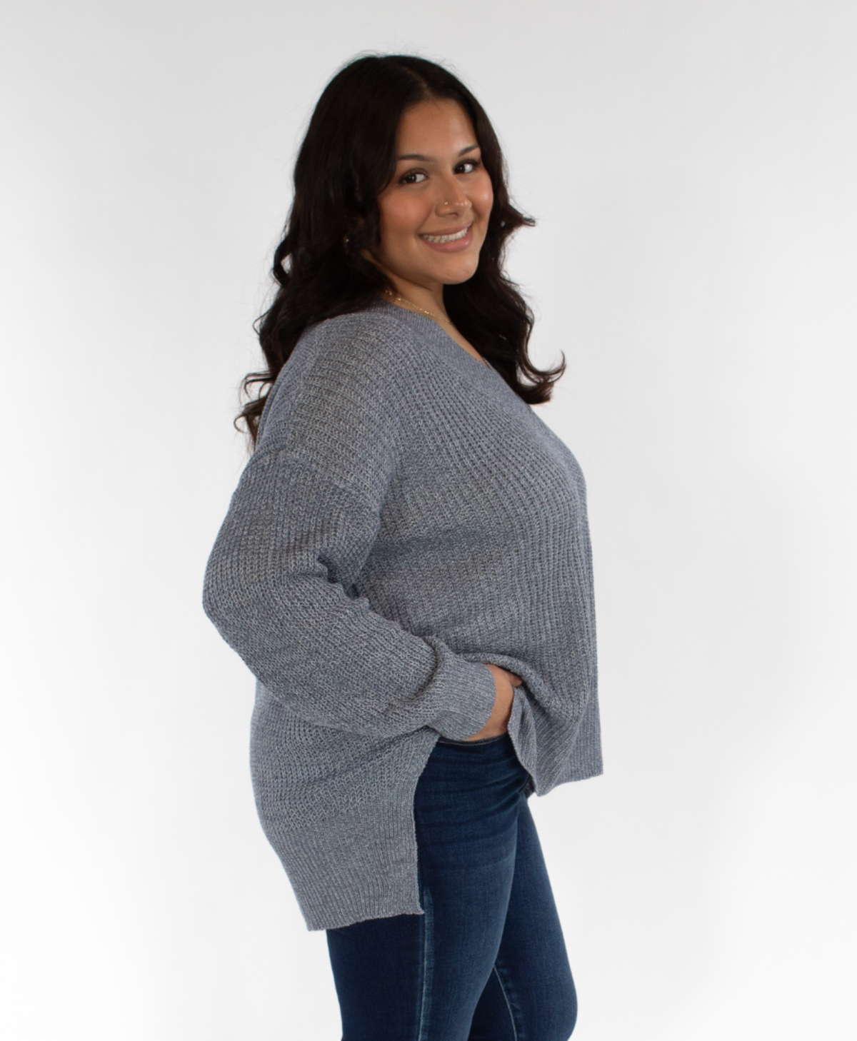 Woman turned to her side wearing a blue sweater and blue jeans on a white background