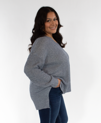 Woman turned to her side wearing a blue sweater and blue jeans on a white background