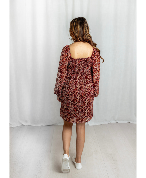 Woman wearing a red floral dress in front of a curtain backdrop