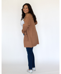 Women side view wearing a brown color cardigan with a white tank top and jeans on a white background