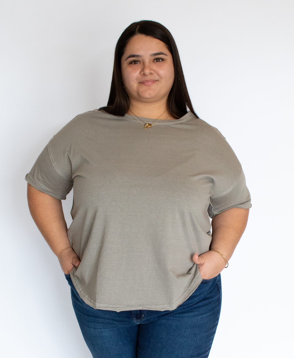 Woman wearing a gray t-shirt with exposed seam detailing and blue jeans against a white background