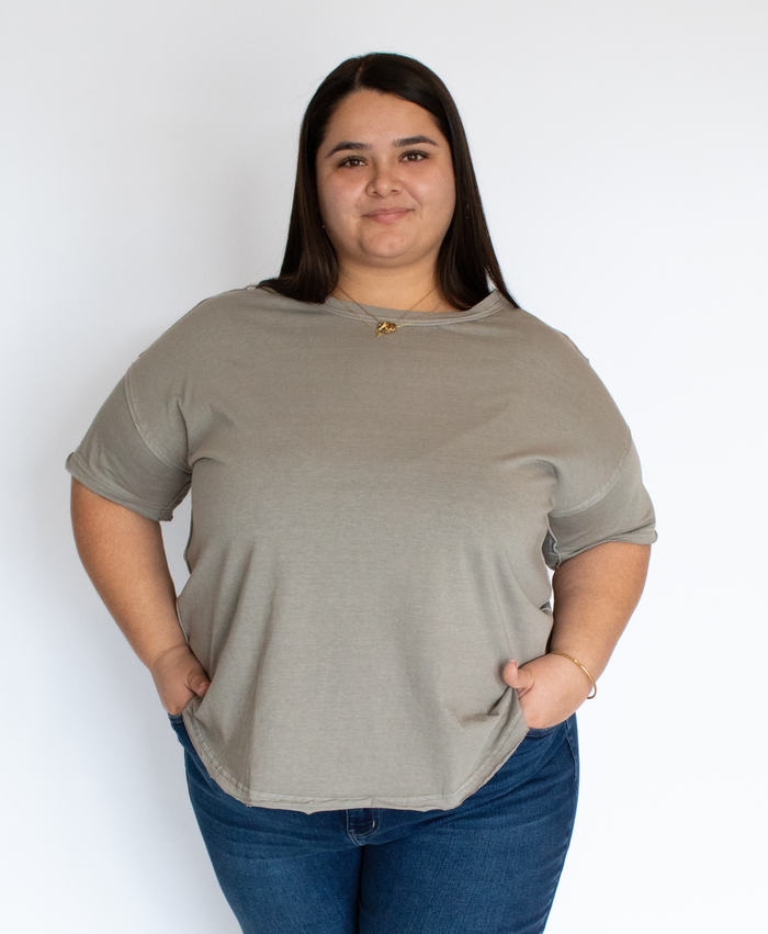 Woman wearing a gray t-shirt with exposed seam detailing and blue jeans against a white background