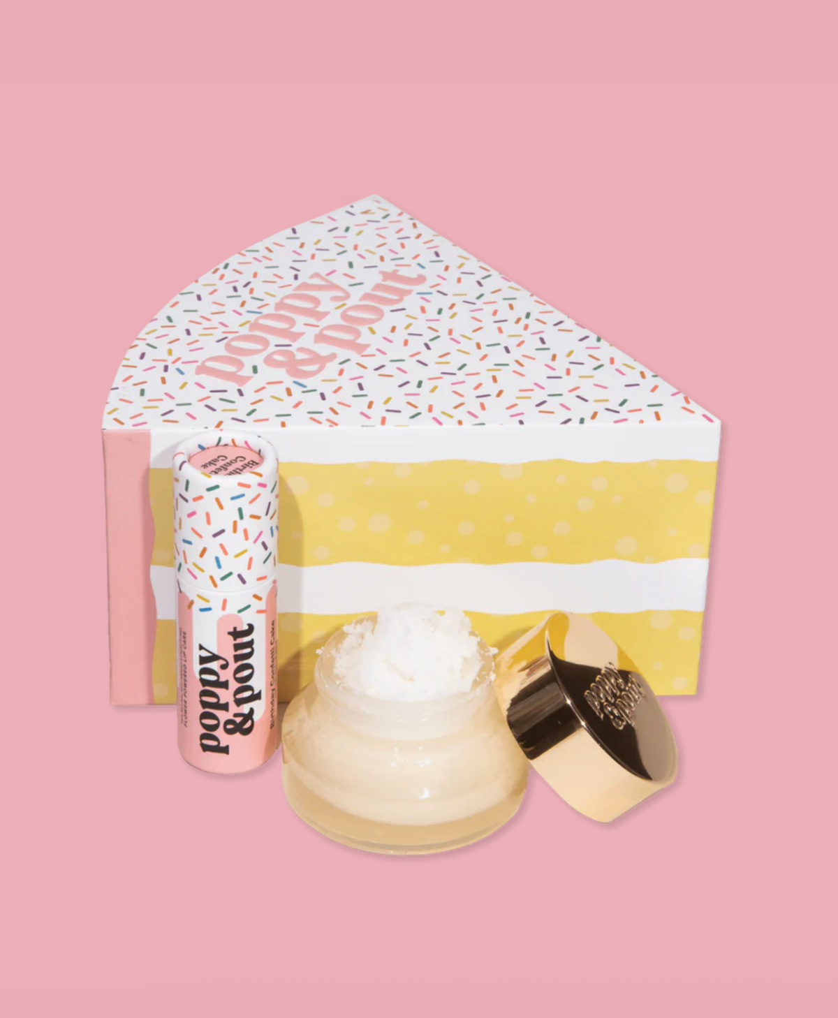 Product packaging with a cake slice-shaped box, lip balm, and lip scrub jar on a pink background