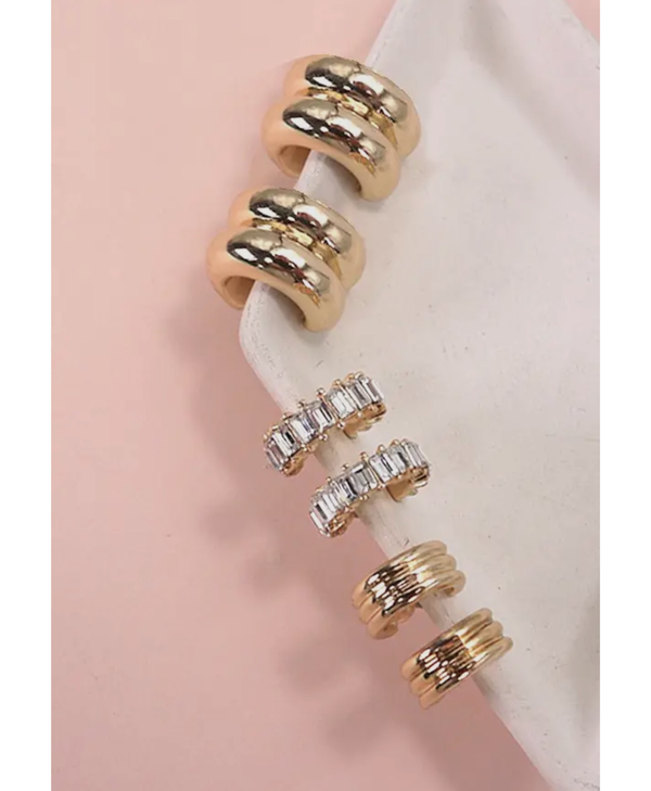 Trio Set of huggie gold earrings on the edge of a white plate with a pink background