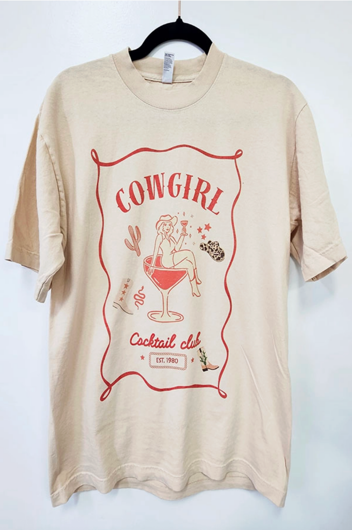Beige t-shirt with 'Cowgirl Cocktail Club' graphic on a white background