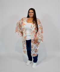 Woman wearing a floral kimono over a white top and blue jeans on a plain background