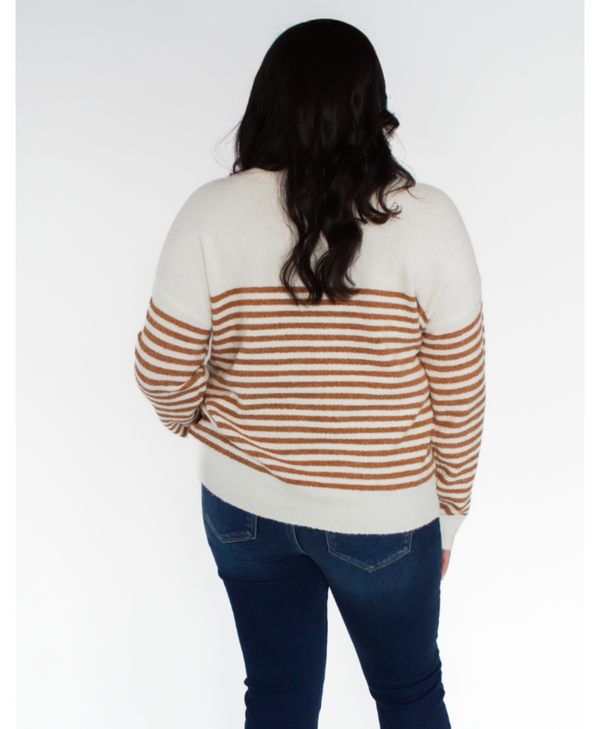 Person wearing a striped sweater and jeans facing a white background