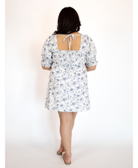 Back of a woman wearing a white with blue floral dress on a white background
