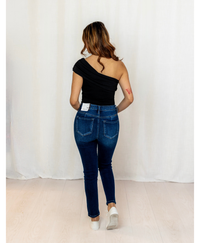 Back of woman wearing a one shoulder black top with jeans on a plain background
