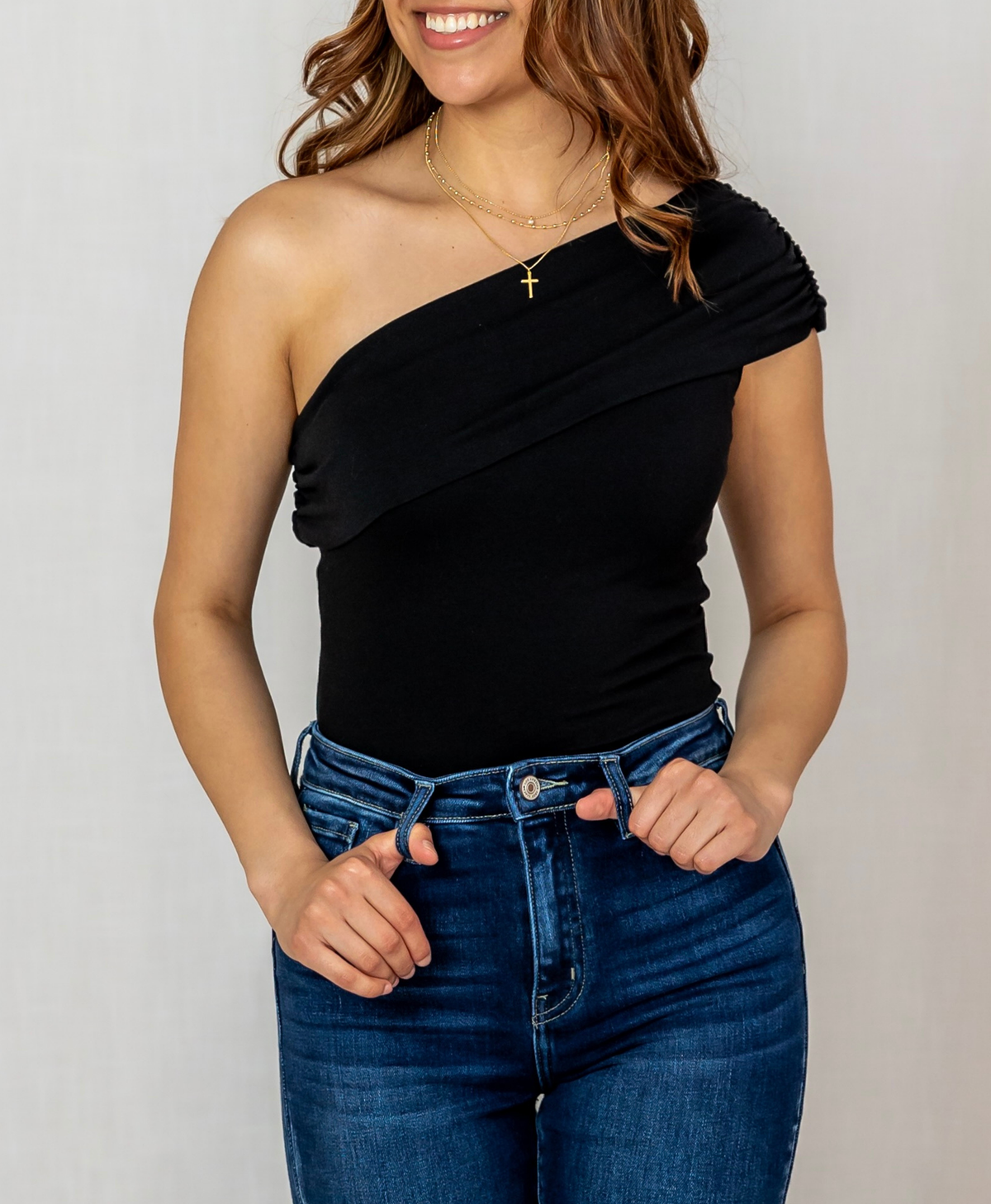 Woman wearing a black one-shoulder top and blue jeans against a plain background