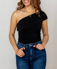 Woman wearing a black one-shoulder top and blue jeans against a plain background
