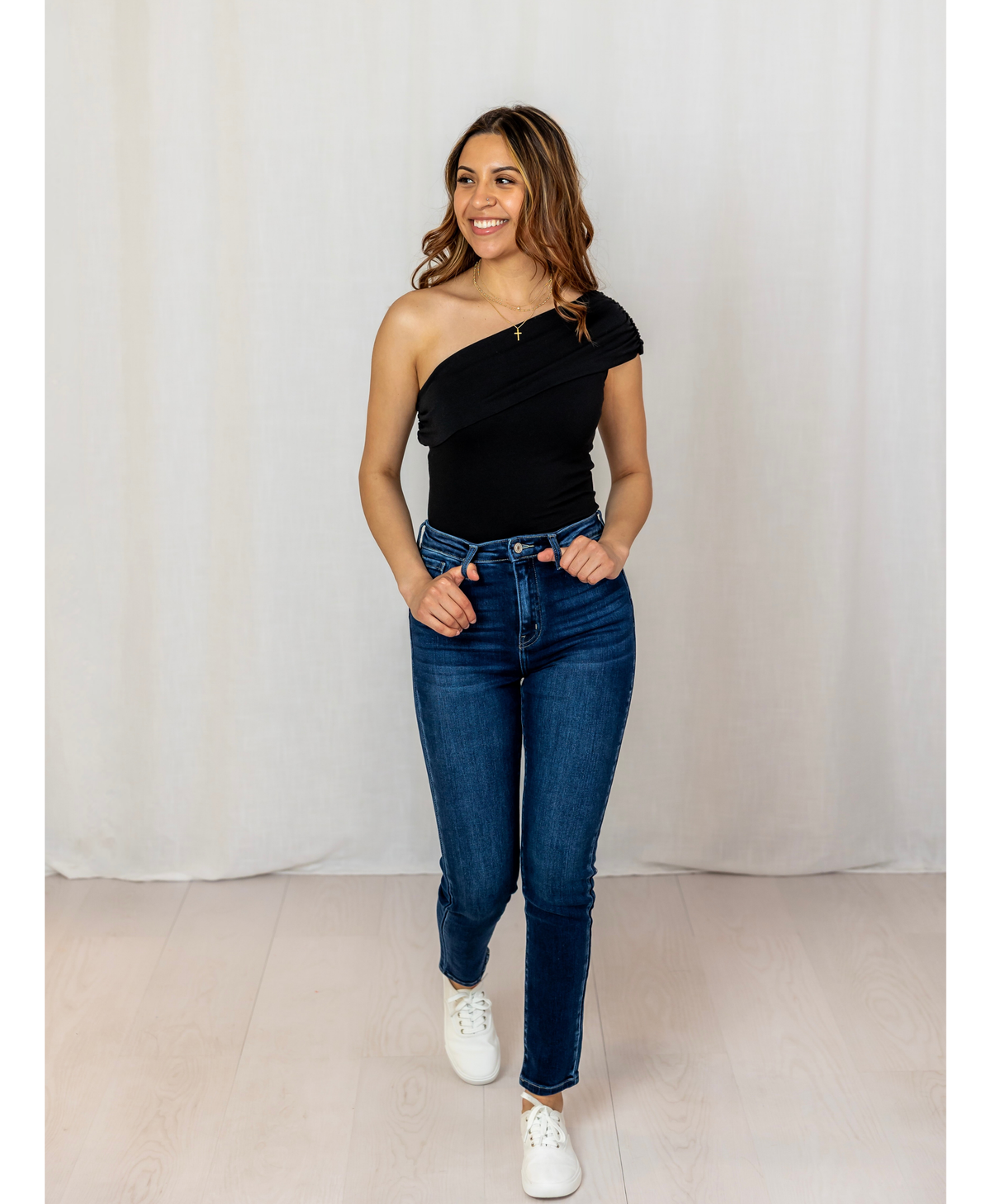 Women wearing a black one shoulder top with jeans on a white background
