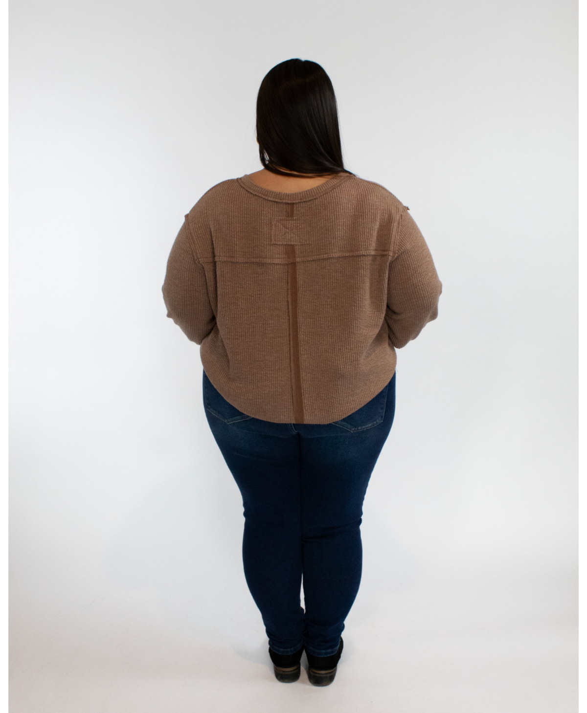 Person wearing a brown long sleeve and dark blue jeans on a white background