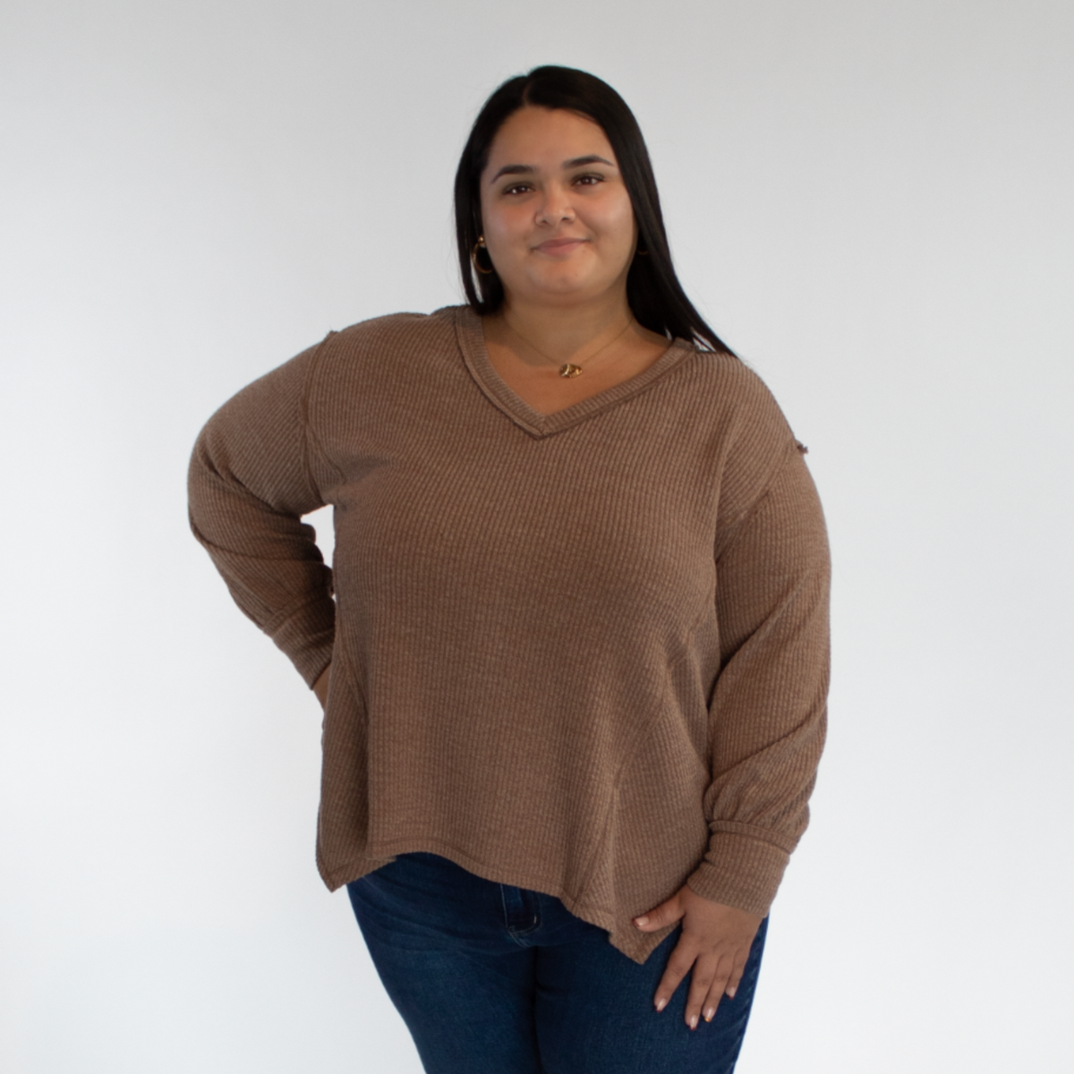 Person wearing a brown long sleeve and blue jeans against a white background