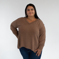 Person wearing a brown long sleeve and blue jeans against a white background