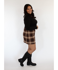 Woman wearing a black top and brown plaid skirt with black boots on a white background
