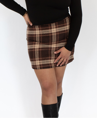 Closer view of the woman wearing a black top and brown plaid skirt with knee-high boots on a white background