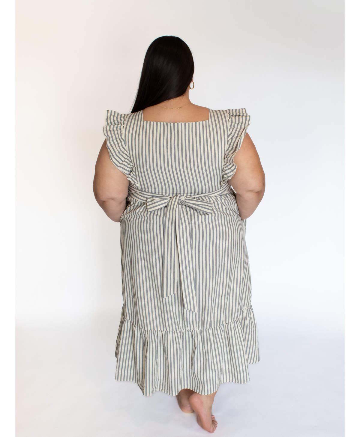 Back of woman wearing a striped full length cream colored dress with ruffle-trimmed short sleeves  against a white background