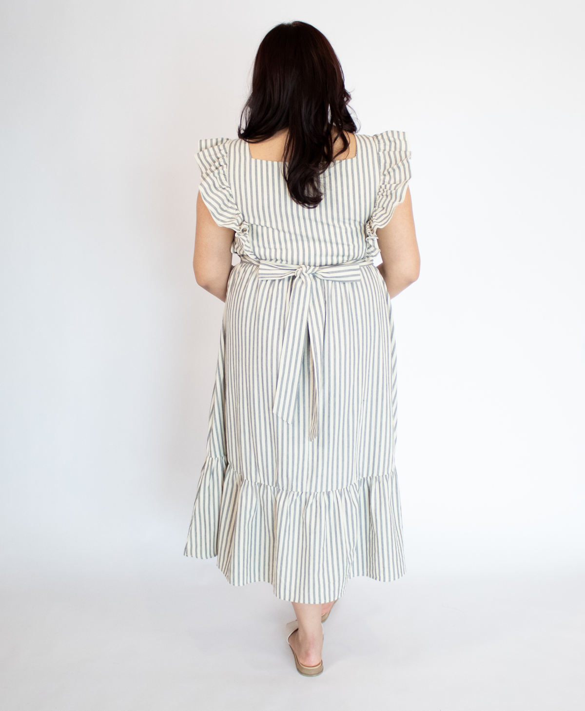Back of woman wearing a striped full length cream colored dress with ruffle-trimmed short sleeves  against a white background