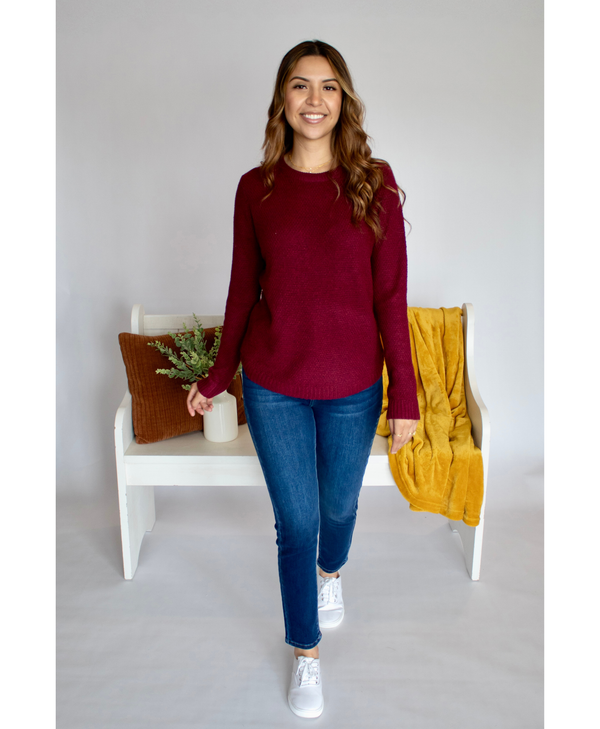 Woman wearing a burgundy long sleeve and blue jeans standing in front of a decorated bench