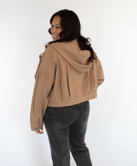 Woman wearing a cropped beige jacket on with black jeans on a white background