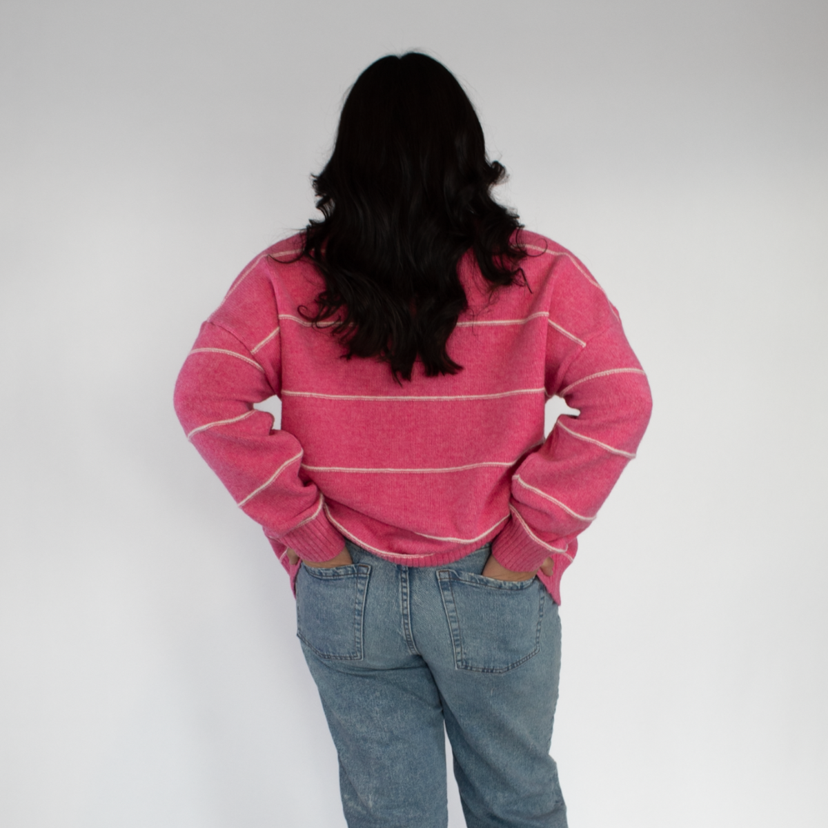 Person wearing a pink striped sweater and blue jeans on a white background