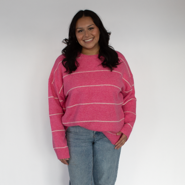 Person wearing a pink striped sweater and blue jeans against a white background
