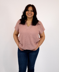 Woman wearing a pink split neckline top and blue jeans against a white background