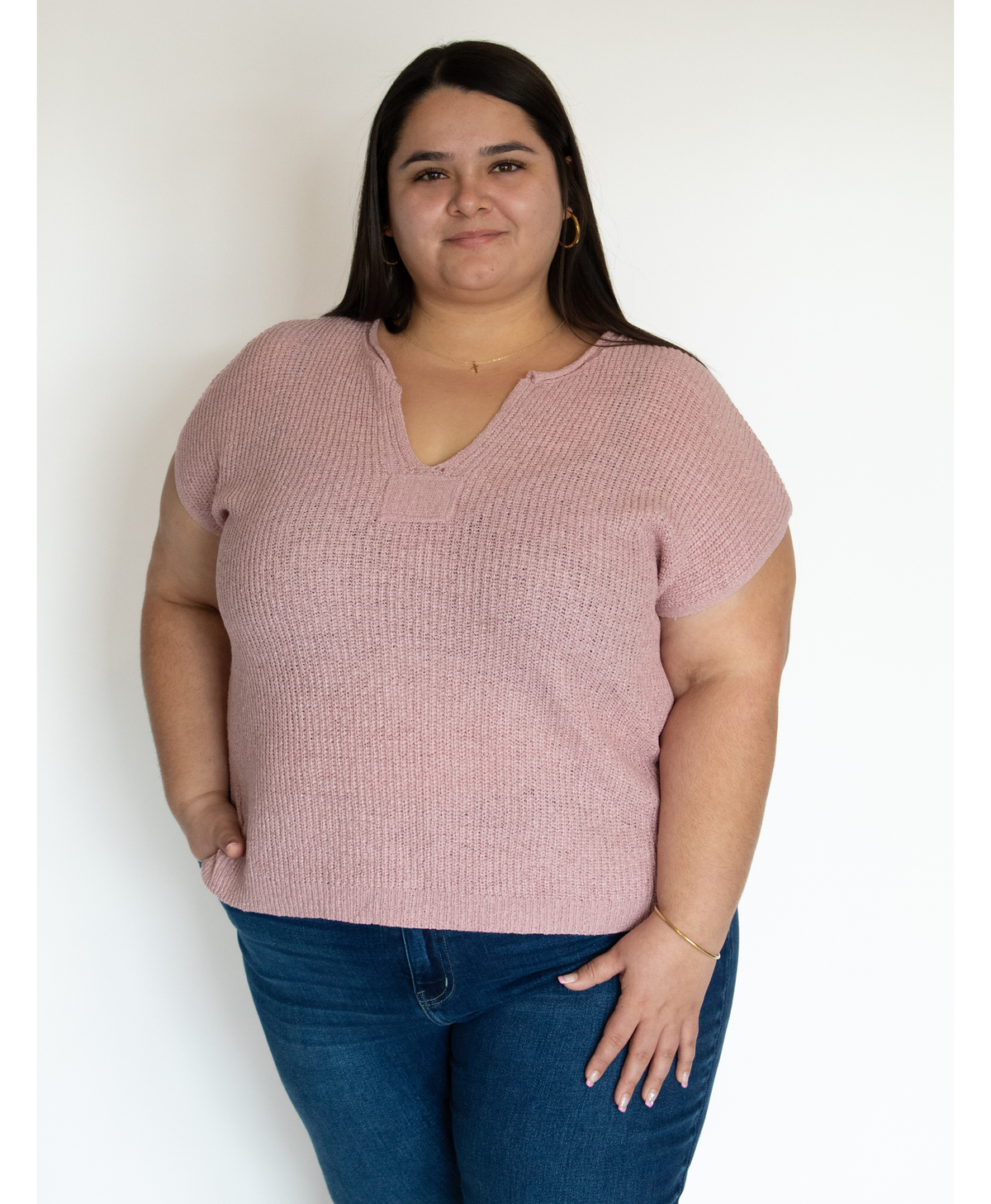 Woman wearing a pink split neckline top and blue jeans against a white background