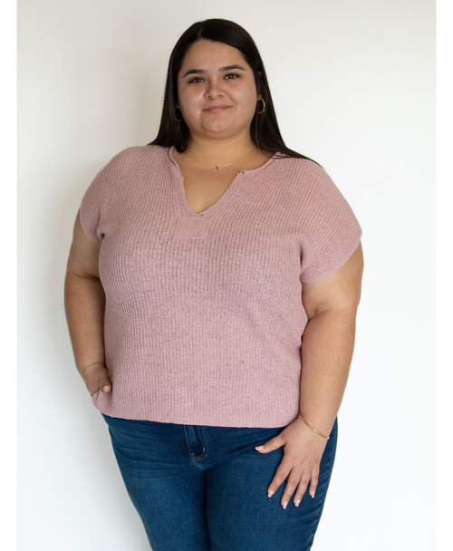 Woman wearing a pink split neckline top and blue jeans against a white background