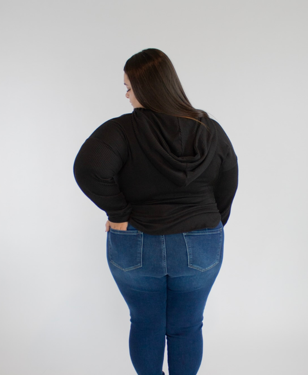Back view of person wearing a black hoodie and blue jeans against a white background