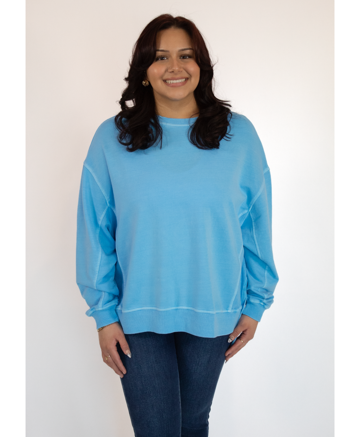 Woman wearing a light blue sweatshirt and dark jeans against a white background