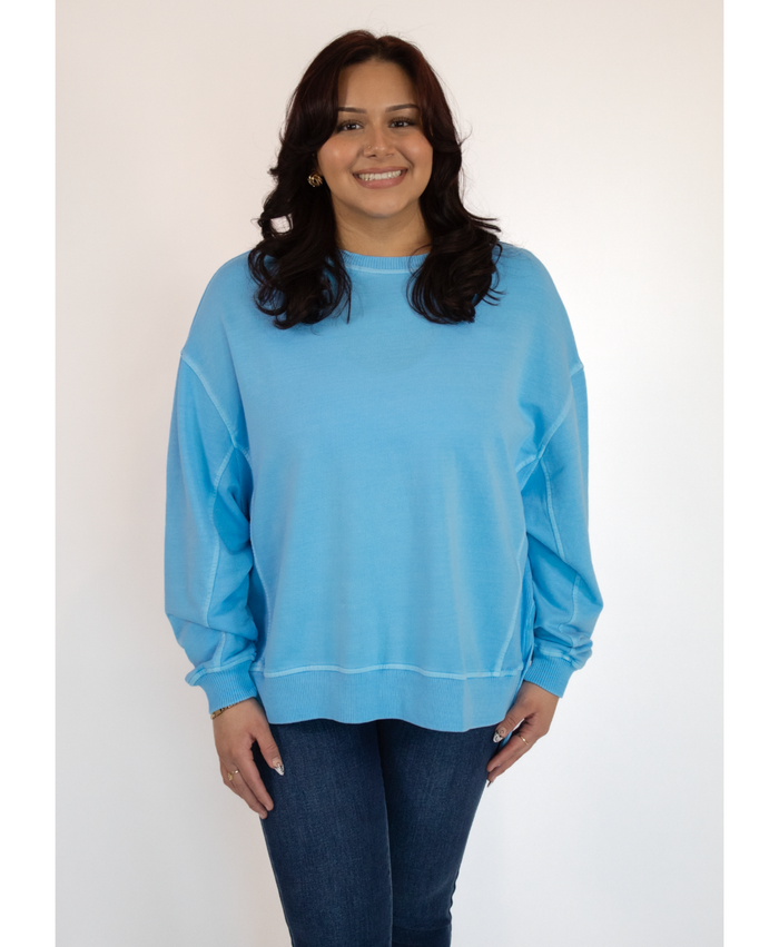 Woman wearing a light blue sweatshirt and dark jeans against a white background