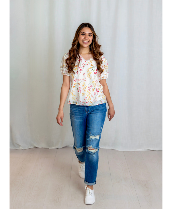 Woman wearing a floral blouse and blue jeans against a white curtain background