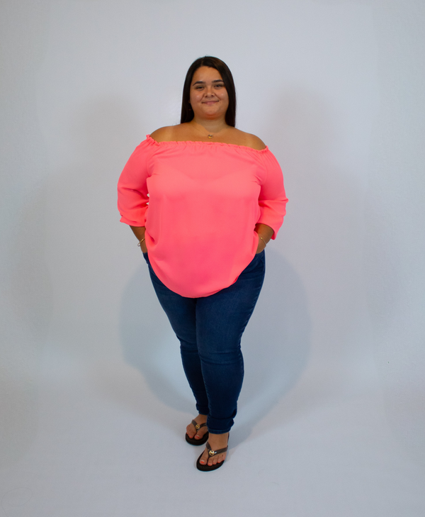 Woman wearing a neon pink off-shoulder top and dark blue jeans on a white background