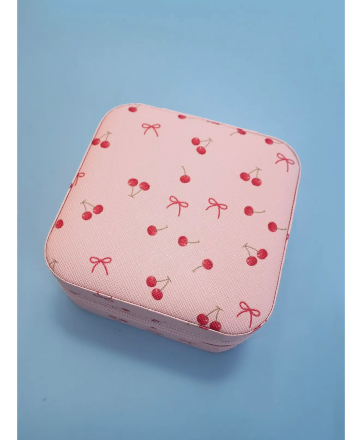Pink travel jewelry box with red bows and cherries on it on a blue background 