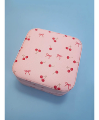 Pink travel jewelry box with red bows and cherries on it on a blue background 