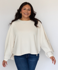 Woman wearing a cream sweater and blue jeans against a white background