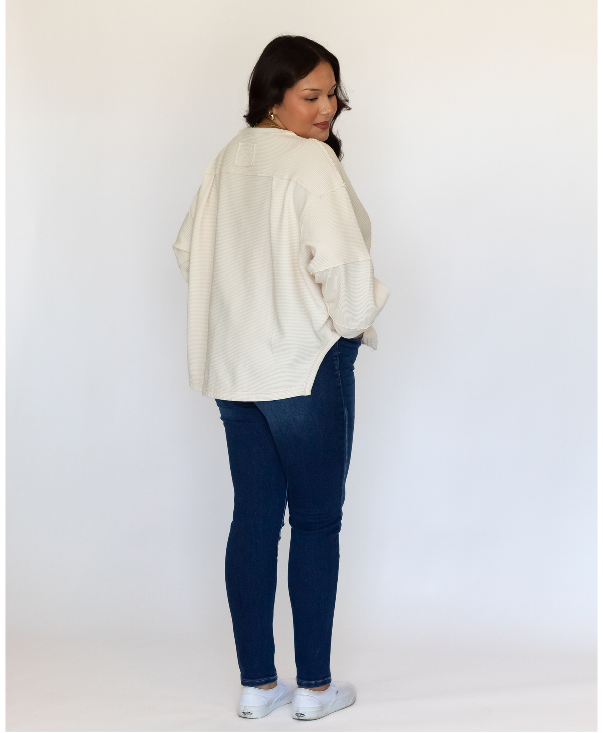 Side view of women wearing a white sweater with jeans on a white background