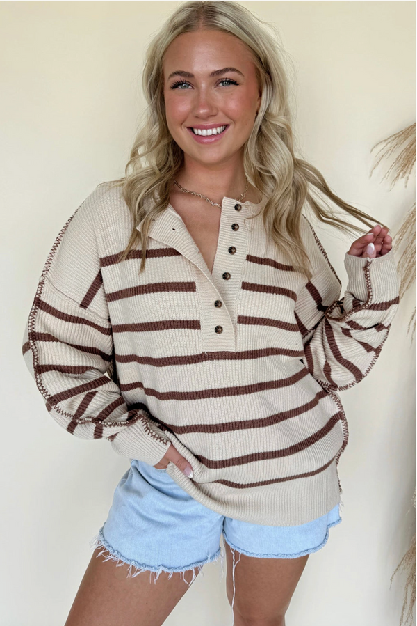 Woman wearing a beige and brown striped sweater with light blue shorts against a neutral background